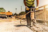 Close-up of manual worker using jackhammer and repairing road.