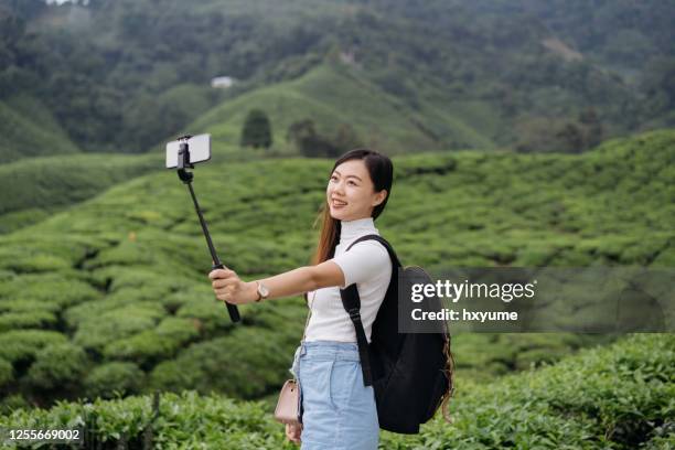 jonge aziatische vrouw die theeplantage onderzoekt en selfie met slimme telefoon neemt - selfiestick stockfoto's en -beelden