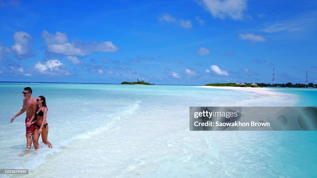 Happy couple walking hand in hand on the pearly white sea shore of a sandbank.