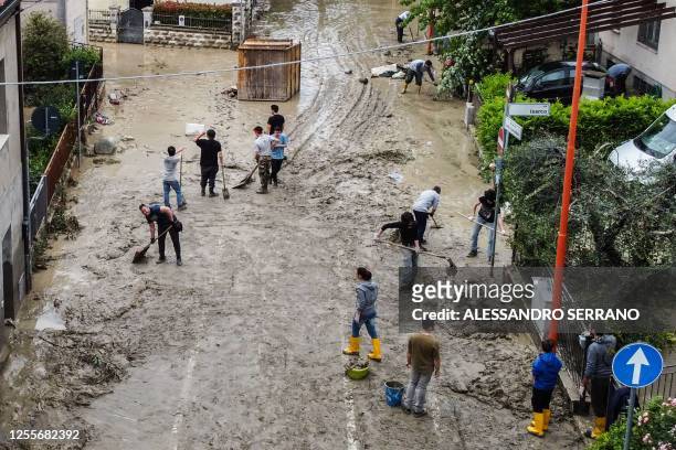 An aerial view taken on May 18, 2023 shows residents clearing mud from a street in the town of Cesena after heavy rains caused flooding across...