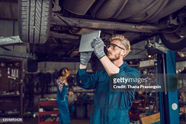 car mechanic using digital tablet in repair garage - auto transmission stockfoto's en -beelden