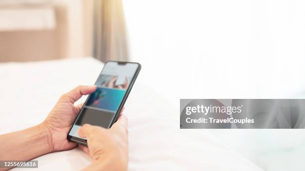 front view of female hands holding smartphone while lying in bed having rest watching videos online with copy space for your promotional content. woman doing online shopping at home in bedroom - branded content stock pictures, royalty-free photos & images