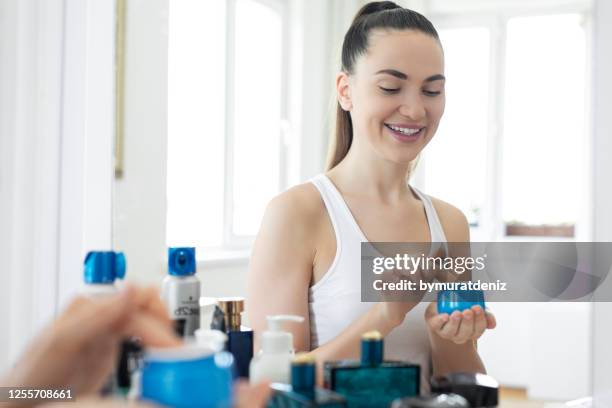 young woman applying face cream at home - cosmetic jar imagens e fotografias de stock