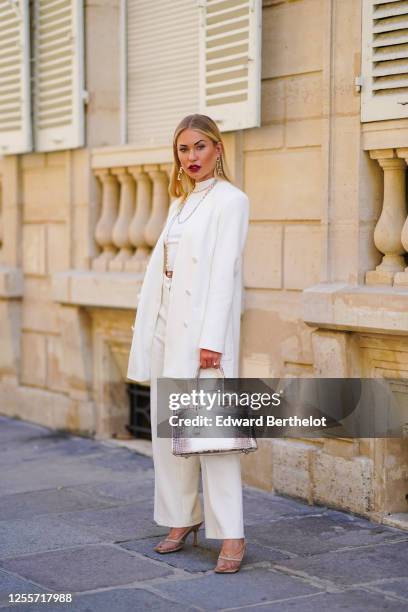 Lexi Fargo wears Chanel large golden earrings, a Chanel long necklace, a white cropped top, a white oversized blazer jacket from Zara, white pants...