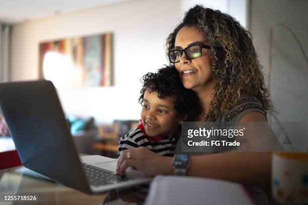 mujer madura trabajando en casa, llevando a su hijo pequeño - monoparental fotografías e imágenes de stock
