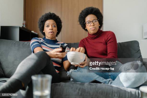 black twin sisters watching tv together at home - twin stock pictures, royalty-free photos & images
