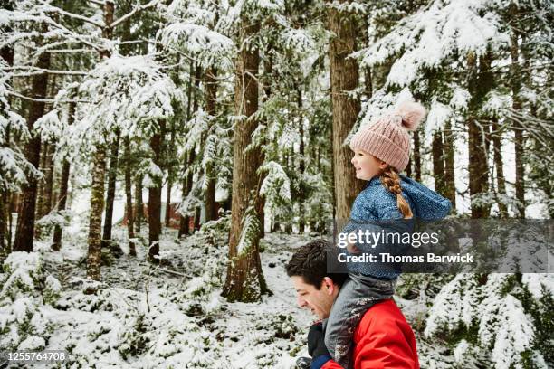 father carrying daughter on shoulders during walk in forest - family snow stock pictures, royalty-free photos & images