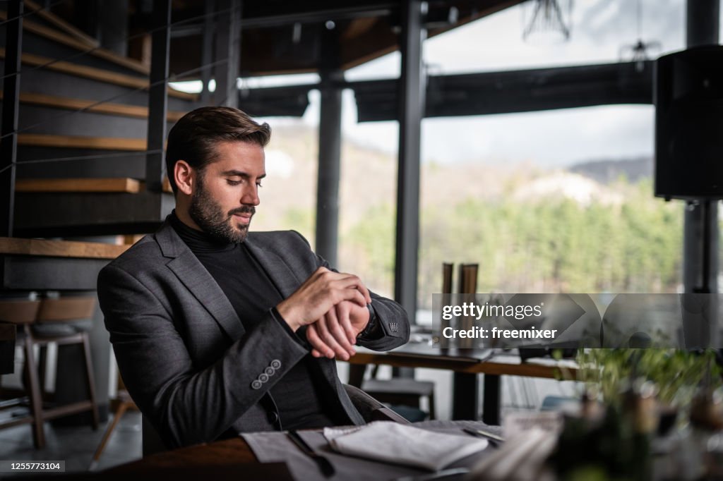 Jonge zakenmanzitting in restaurant en het kijken naar horloge
