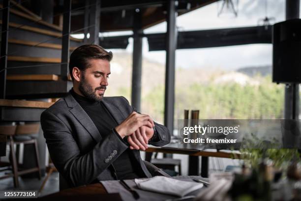 jonge zakenmanzitting in restaurant en het kijken naar horloge - goed gekleed stockfoto's en -beelden