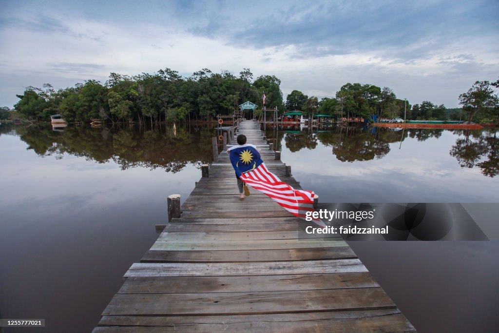 A Boy Running With A Long Malaysian Flag on a Pier / Jetty