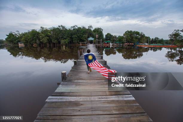 a boy running with a long malaysian flag on a pier / jetty - malaysia flag stock pictures, royalty-free photos & images