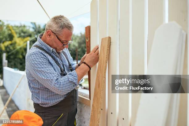 konzentrierter senior-handwerker misst eine holzplanke mit einem niveau - zaun stock-fotos und bilder