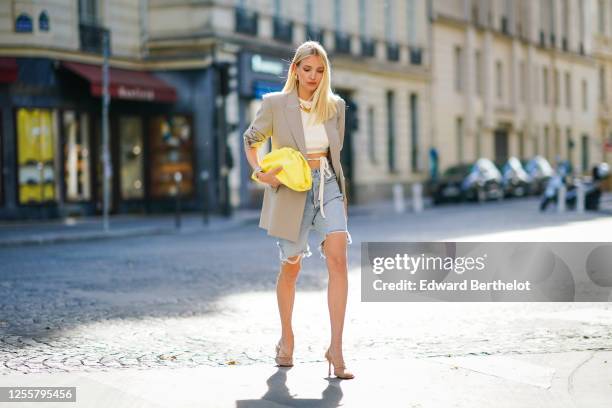 Leonie Hanne wears golden earrings, a golden necklace, a white cropped top from Orseund Iris, a gray oversized long blazer jacket from Frankie Shop,...