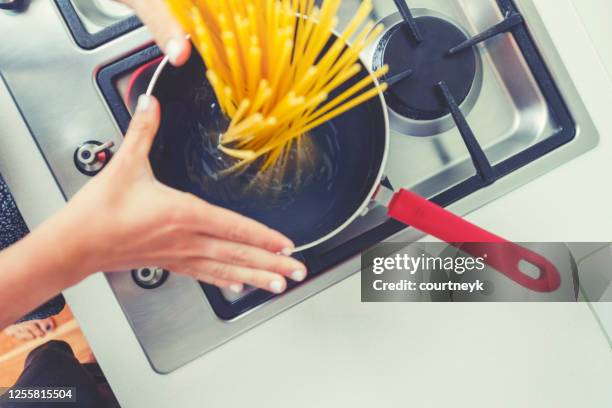 woman dropping pasta into boiling water. - boiling pasta stock pictures, royalty-free photos & images