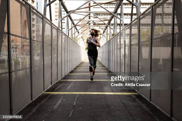 Young female runner doing training with face mask on bridge in urban settings