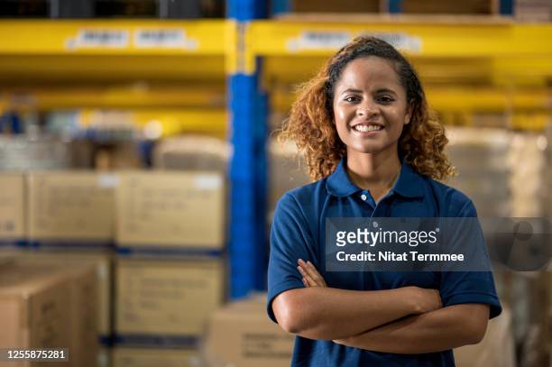 portrait of smiling african female warehouse manager with arms crossed in distribution warehouse center.  supply chain, warehouse management. - camisa pólo imagens e fotografias de stock