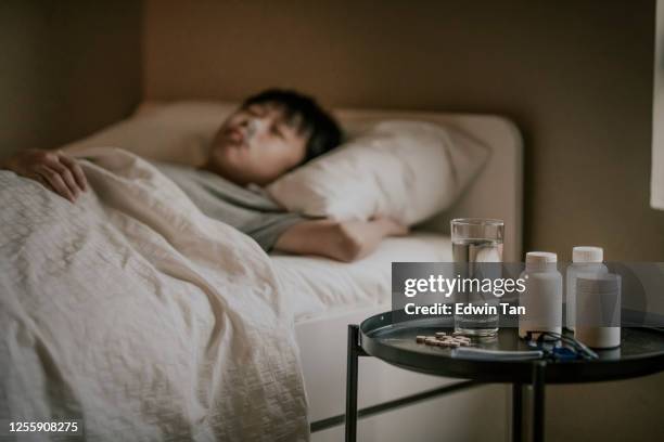 ein asiatischer chinesischer kranker junge, der auf dem bett liegt und ein thermometer im mund hat, das die körpertemperatur misst - hot boy body stock-fotos und bilder