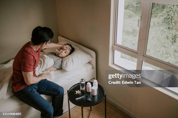 an asian chinese man measuring his son body temperature with thermometer and touching his son's forehead worried - hot boy body stock pictures, royalty-free photos & images