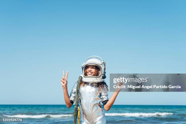 a smiling girl on the beach in an astronaut suit with the victory sign in her hands - child in space suit stock pictures, royalty-free photos & images