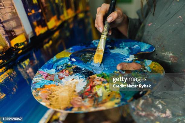 young caucasian woman mixes paints on a palette at home art studio - paintbrush palette stock pictures, royalty-free photos & images