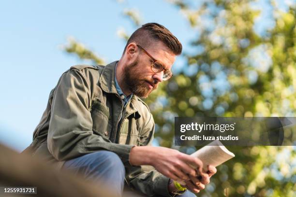 man sitting in a park reading a book - reading glasses stock pictures, royalty-free photos & images
