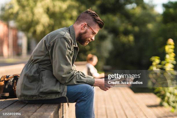 homme s’asseyant dans un parc affichant un livre - livre broché photos et images de collection