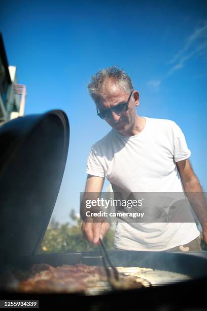 genießen sie einen grill mit der familie im hinterhof, fleischgerichte am grill, vater und sohn grillen im garten - bbq tools stock-fotos und bilder