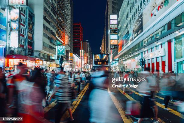 blurred motion of a crowd of busy commuters crossing the street in downtown financial district against contemporary corporate skyscrapers and city traffic, with multi-coloured commercial signs in the background at night - asien metropole nachtleben stock-fotos und bilder