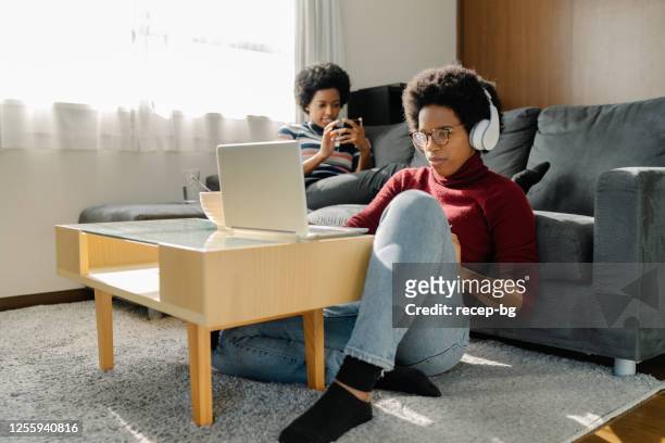 dos mujeres negras pasan su tiempo usando computadora portátil y teléfono inteligente cómodamente en casa - twin fotografías e imágenes de stock