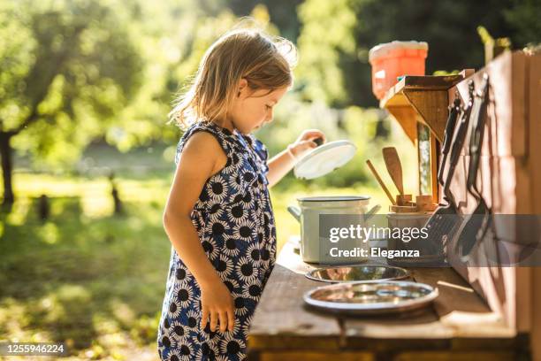 little girl wearing dress, playing and cooking in her little kitchen outdoors - outdoor kitchen stock pictures, royalty-free photos & images