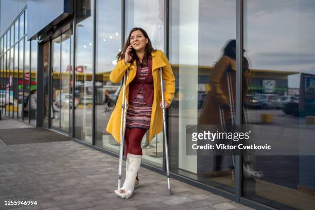 mujer con pie de yeso hablando por teléfono - crutches fotografías e imágenes de stock