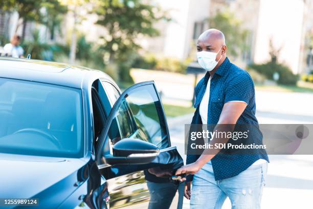 man wears mask to drive car during coronavirus epidemic - car isolated doors open stock pictures, royalty-free photos & images