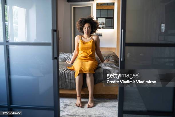 lonely young woman sitting on bed in bedroom alone - yellow dress stock pictures, royalty-free photos & images