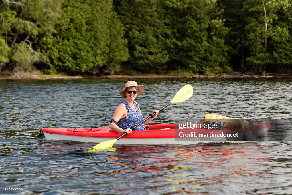 50 + mulher andando de caiaque em um lago.