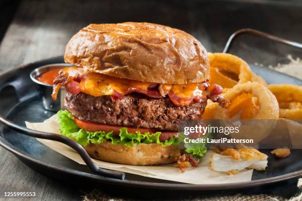 bacon and cheddar burger with lettuce, tomato and thick cut onion rings on a toasted onion bun - onion ring stock pictures, royalty-free photos & images