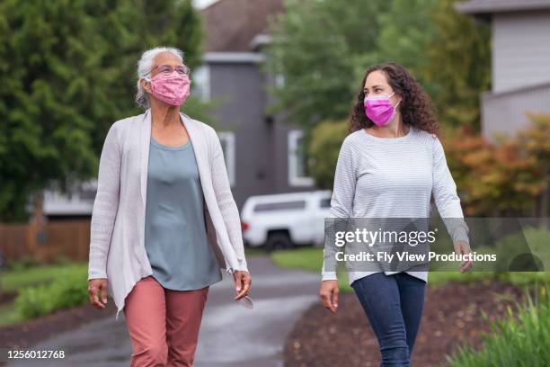 two women wearing protective face masks enjoying the outdoors during coronavirus - social distancing mask stock pictures, royalty-free photos & images