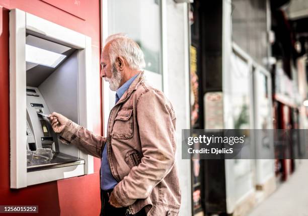 homme aîné insérant une carte de crédit dans le distributeur automatique de atm. - dab photos et images de collection