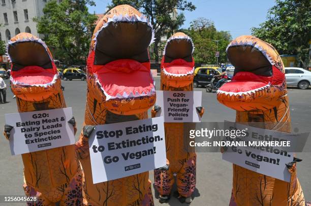 Supporters of People for the Ethical Treatment of Animals and Aashray Foundation, wearing inflatable dinosaur costumes hold placards to make an...