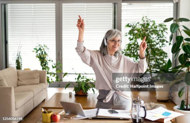 active senior architect with headphones at the table in home office, taking a break. - senior man dancing on table stock-fotos und bilder