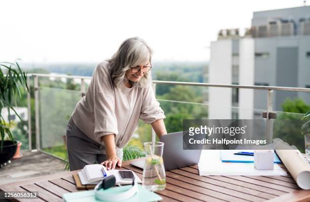 Active senior architect with laptop in home office, working outdoors on balcony.