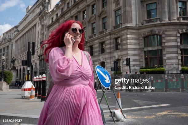 Woman with red hair and wearing a pink dress walks and talks on her phone in the City of London, the capital's financial district, on 18th May 2023,...