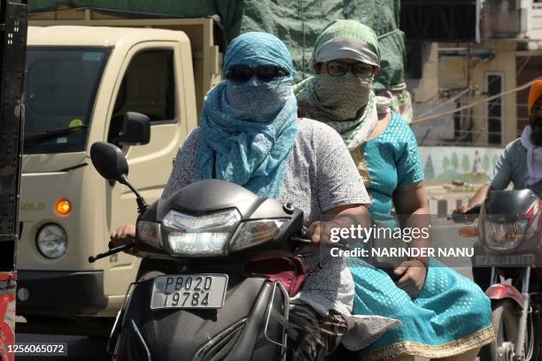 Women riding a scooter cover their faces with scarfs during a hot summer day in Amritsar May 19, 2023.