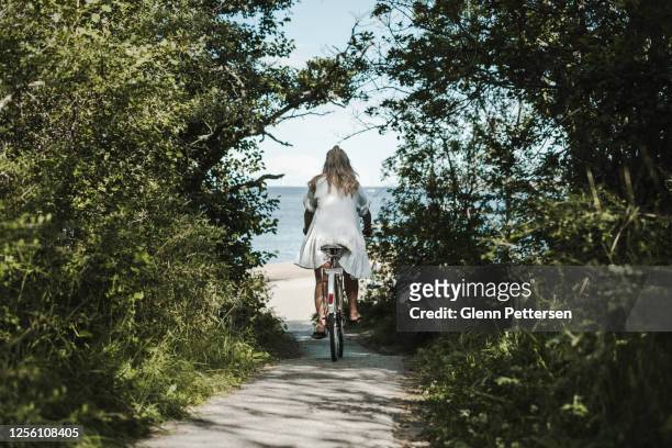 young woman biking towards ocean - scandinavian descent stock pictures, royalty-free photos & images