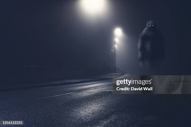 a monster with glowing eyes, floating above an empty road on a foggy winters night - monsters stock pictures, royalty-free photos & images