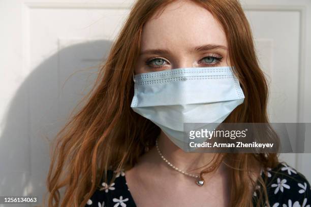 a serious young woman wearing protective face mask and looking at camera - green eyes - fotografias e filmes do acervo