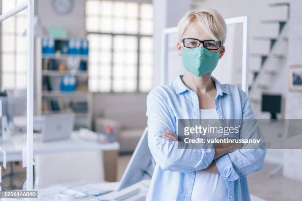 mid adult woman wearing protective face mask in the office for safety and protection during covid-19 - cloth face mask stock pictures, royalty-free photos & images