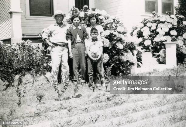 Family of four Japanese American famers stand in front of their home farm, which has crops in the front yard, in Southern California, circa 1940.