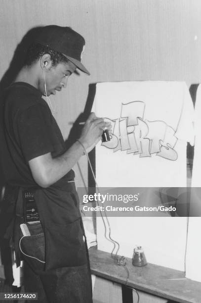 Young African-American airbrush artist applying paint in a graffiti style onto a t-shirt, San Francisco, California, San Francisco, California, 1980....