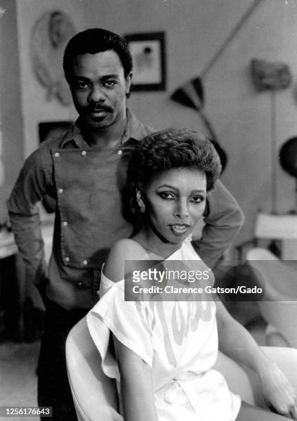 Female African-American model striking a pose while sitting in a chair, with a man standing behind her, San Francisco, California, 1990. .