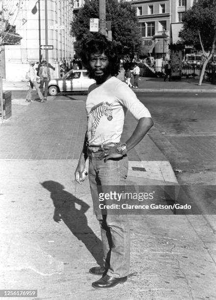 Black and white photograph of a young African-American man, full length, standing, posing, on a city sidewalk, with long hair, wearing a zebra print...